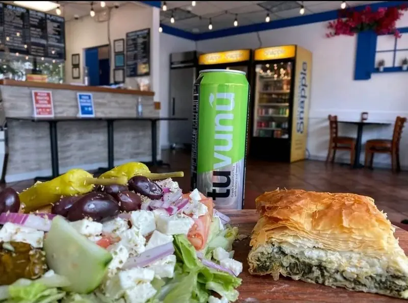 Greek salad and a square of spanakopita on the counter, drink coolers behind
