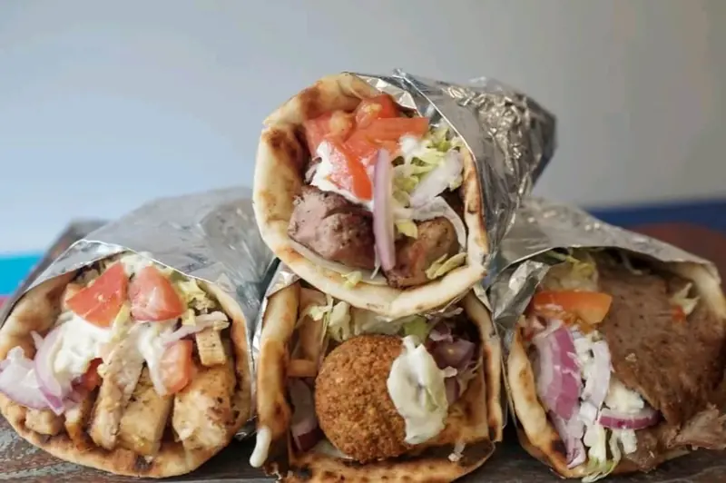 Pile of foil-wrapped gyro and falafel pitas
