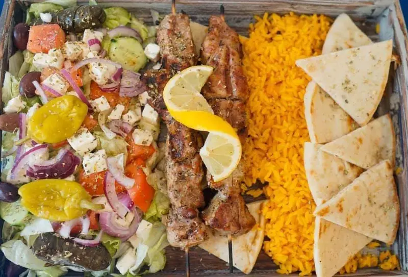 Souvlaki skewers over yellow rice with pita, salad and a lemon wedge